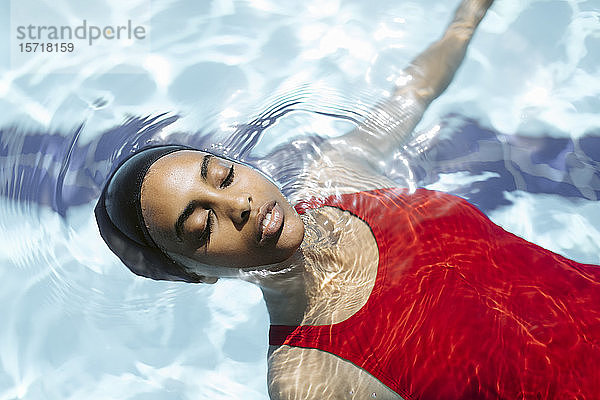 Porträt einer jungen Frau mit geschlossenen Augen  die auf Wasser im Schwimmbad schwimmt