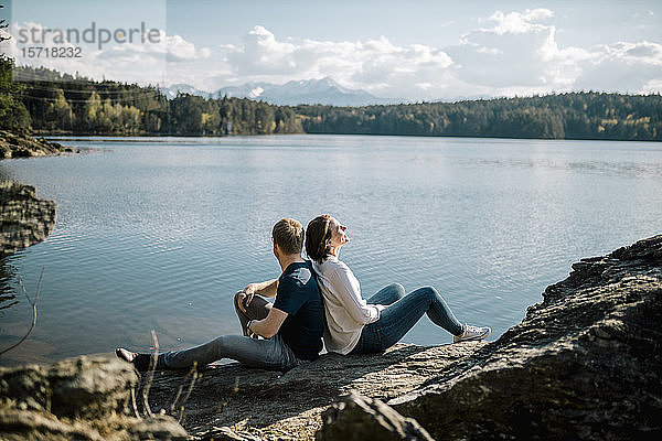 Glückliches Paar sitzt Rücken an Rücken am Seeufer  Forstsee  Kärnten  Österreich