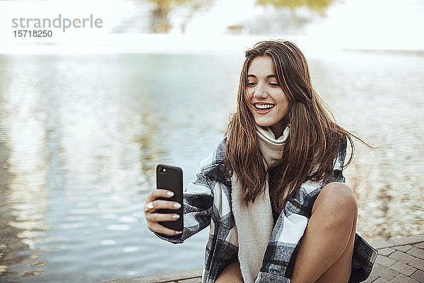 Junge brünette Frau mit Smartphone und Selbstbedienung am See