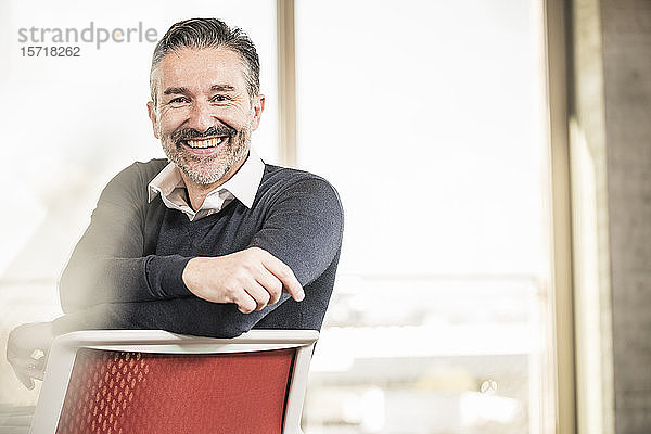 Porträt eines glücklichen reifen Geschäftsmannes  der auf einem Stuhl im Büro sitzt