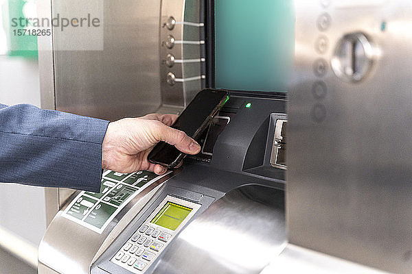 Mann hält Smartphone am Fahrkartenautomaten und bezahlt