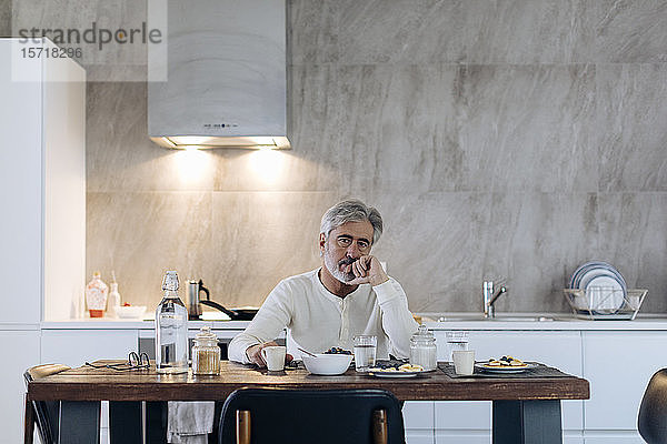 Porträt eines reifen Mannes  der zu Hause in der Küche am Tisch sitzt