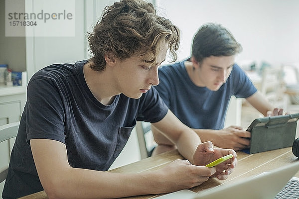 Zwei Jungen im Teenager-Alter benutzen zu Hause Smartphone und Tablet auf dem Tisch