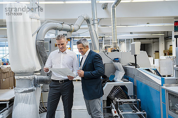Zwei lächelnde Geschäftsmänner diskutieren in einer Fabrik über Papier