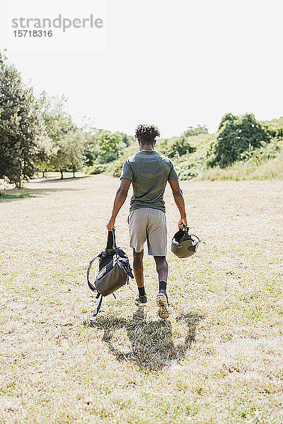 Rückansicht eines jungen Mannes mit Helm und Rucksack beim Spaziergang im Park