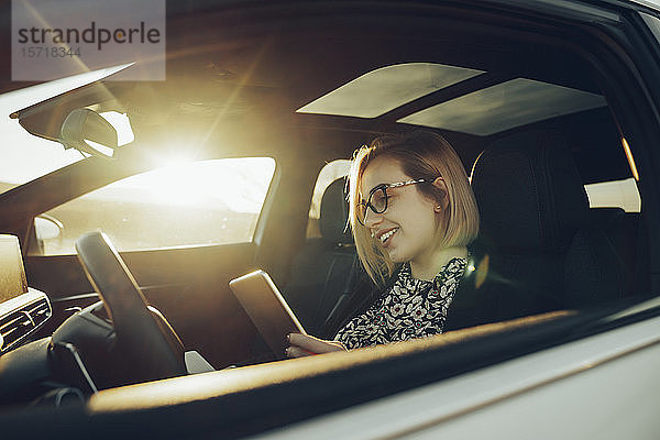 Junge blonde Frau mit Smartphone im Auto