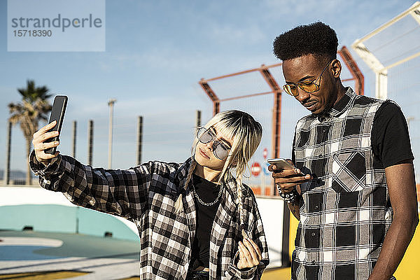 Junge Frau nimmt Selfie mit ihrem Freund  der auf sein Smartphone schaut