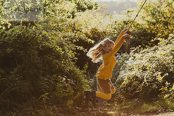 Glückliches kleines Mädchen schwingt auf einer Seilschaukel in der Natur