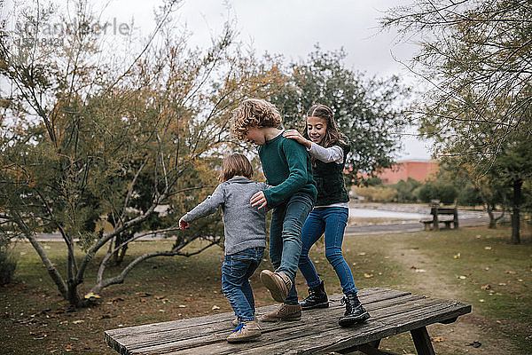 Drei Kinder  die im Herbst auf dem Picknicktisch tanzen und Spaß haben