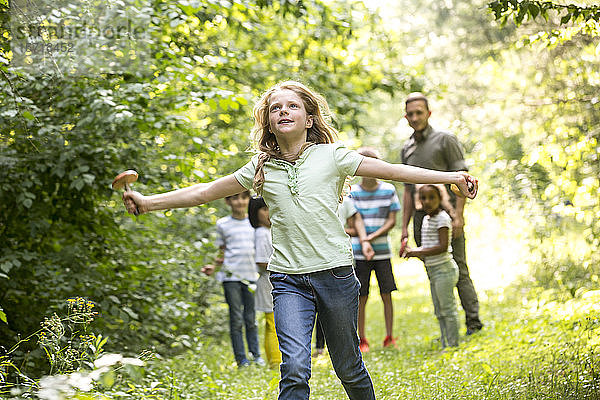 Schulkinder  die mit ihrem Lehrer im Wald spazieren gehen  Mädchen rennt  hält Pilz