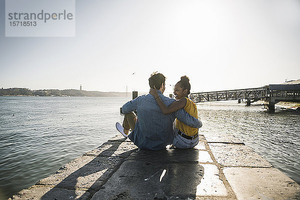 Rückansicht eines jungen Paares  das am Pier am Wasser sitzt  Lissabon  Portugal