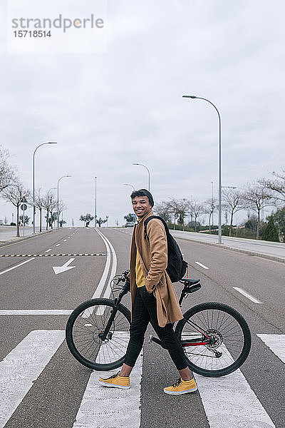 Junger Mann mit Fahrrad überquert eine Straße in der Stadt