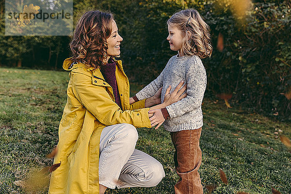 Lächelnde Mutter mit Tochter im Herbst auf einer Wiese