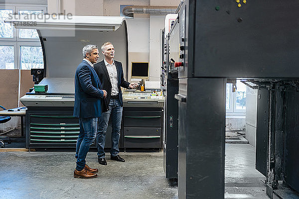 Zwei Geschäftsleute betrachten eine Maschine in einer Fabrik