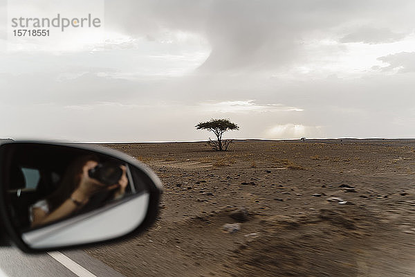 Tragflächenspiegel mit Spiegelung einer Frau im Auto  die mit der Kamera eine Landschaft fotografiert  Fez  Marokko
