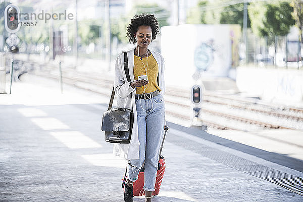 Lächelnde junge Frau mit Handy und Kopfhörern am Bahnhof