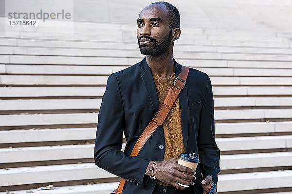 Porträt eines bärtigen jungen Geschäftsmannes mit Smartphone und Kaffee  um auf Distanz zu gehen