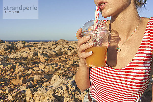 Junge Frau trinkt Saft am felsigen Strand