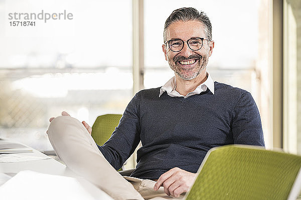 Porträt eines lächelnden reifen Geschäftsmannes  der im Büro am Schreibtisch sitzt