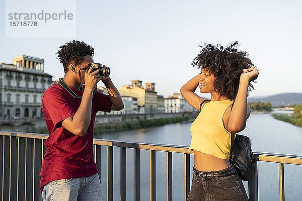 Junger Mann fotografiert seine Freundin auf einer Brücke über dem Arno bei Sonnenuntergang  Florenz  Italien