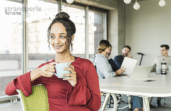 Lächelnde junge Geschäftsfrau bei einer Kaffeepause während einer Besprechung im Büro