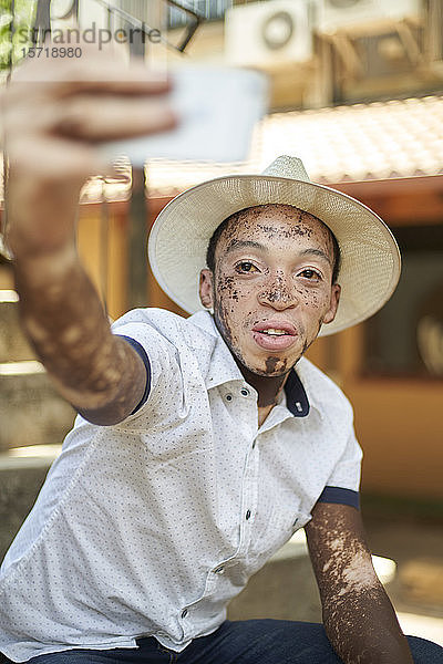 Junger Mann mit Vitiligo  der ein Smartphone benutzt und ein Selfie nimmt
