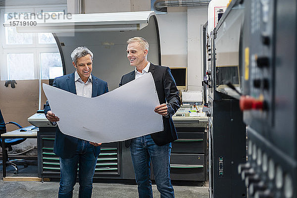 Zwei lächelnde Geschäftsleute diskutieren in einer Fabrik über einen Plan