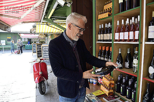 Reifer Mann wählt eine Flasche Wein in einem Weinladen