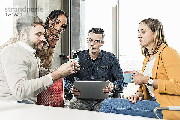Junge Geschäftsleute mit Laptop und Atommodell bei einer Besprechung im Büro