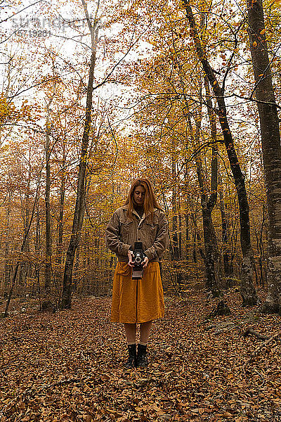 Rothaarige junge Frau fotografiert mit analoger Kamera im Herbstwald