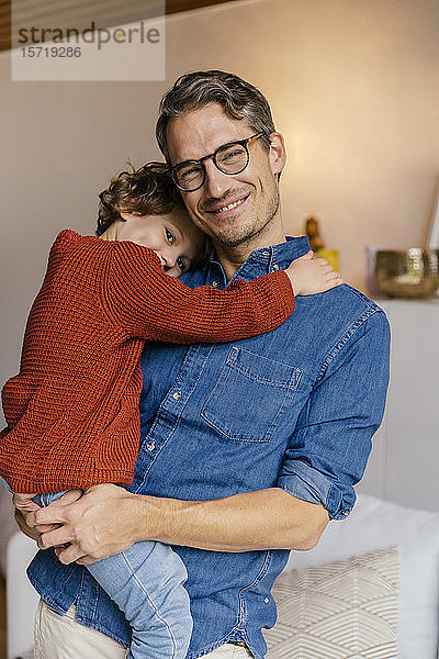 Porträt eines lächelnden Vaters  der seine Tochter zu Hause trägt