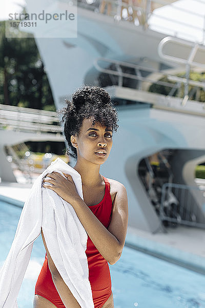 Porträt einer jungen Frau in rotem Badeanzug mit Handtüchern vor einem Pool