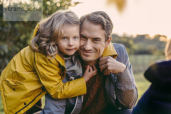 Porträt eines Mädchens  das im Herbst den lächelnden Vater im Freien umarmt