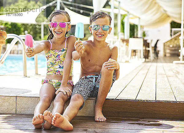 Porträt eines fröhlichen kleinen Mädchens und Jungen mit verspiegelter Sonnenbrille  die ihre Eis am Stiel zeigen