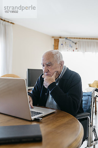 Portrait eines älteren Mannes im Rollstuhl mit Laptop zu Hause