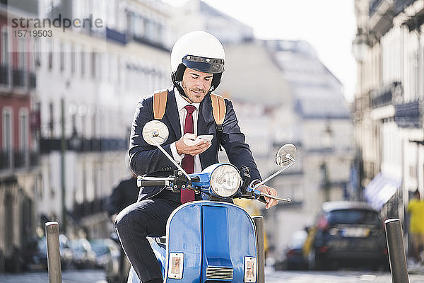 Junger Geschäftsmann auf Motorroller mit Handy in der Stadt  Lissabon  Portugal