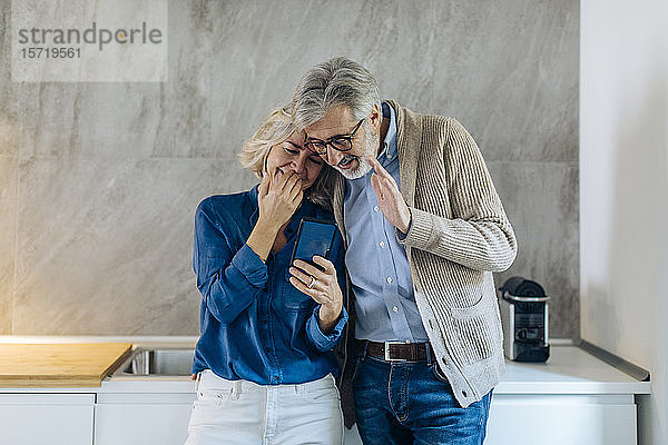 Ein erwachsenes Paar  das zu Hause in der Küche gemeinsam ein Mobiltelefon benutzt