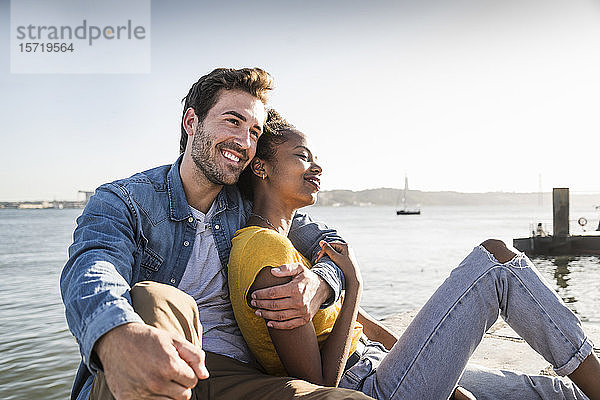 Glückliches junges Paar sitzt am Pier am Wasser  Lissabon  Portugal