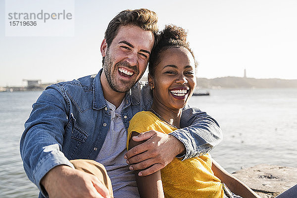 Porträt eines glücklichen jungen Paares am Wasser sitzend  Lissabon  Portugal