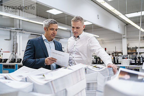 Zwei Geschäftsleute diskutieren in einer Fabrik über Papier