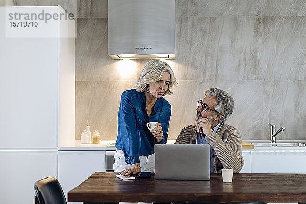 Reifer Mann mit Frau  der zu Hause einen Laptop auf dem Küchentisch benutzt