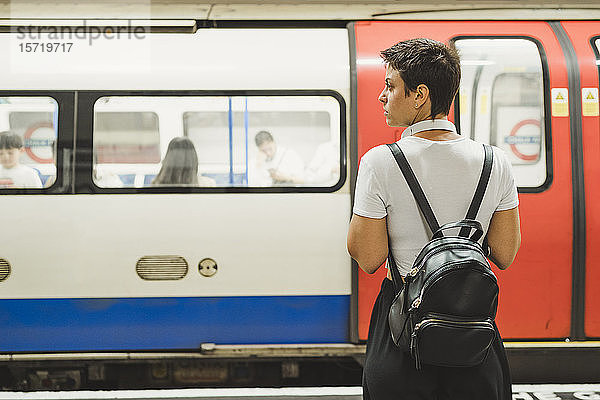 Rückenansicht einer Frau mit Rucksack  die auf dem Bahnsteig der U-Bahn-Station wartet  London  UK