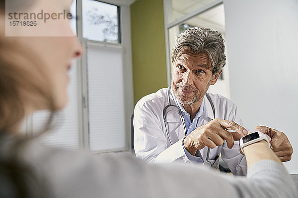 Arzt überprüft Smartwatch einer Patientin in seiner Praxis