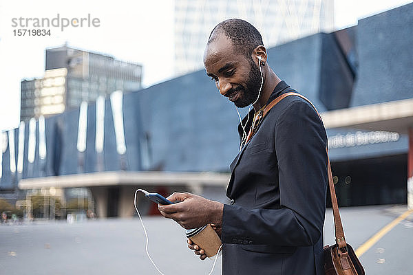 Porträt eines lächelnden jungen Geschäftsmannes mit Kaffee zum Musikhören mit Kopfhörern und Smartphone