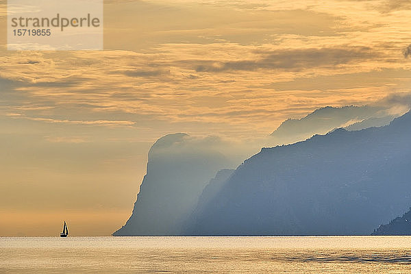 Italien  Trentino  Nago-Torbole  Silhouette eines Segelbootes  das in der Nähe der Küstenklippen des Gardasees im launischen Morgengrauen segelt