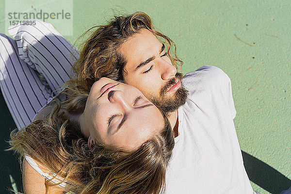 Junges Paar mit geschlossenen Augen entspannt sich Kopf an Kopf im Sonnenlicht