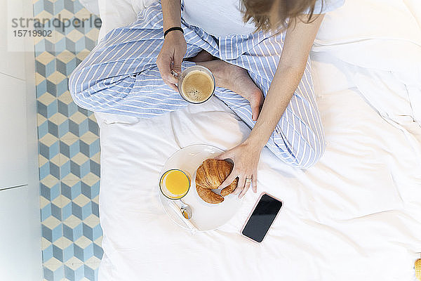 Junge Frau sitzt auf dem Bett und trinkt einen Kaffee
