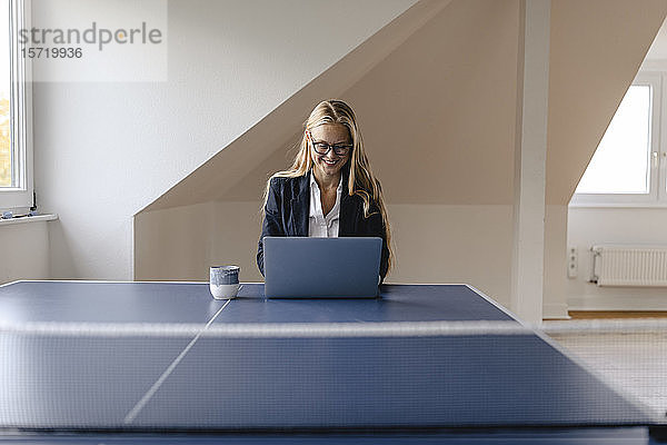 Junge Geschäftsfrau mit Laptop auf Tischtennisplatte im Büro