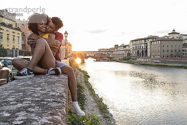 Liebenswertes junges Touristenpaar sitzt bei Sonnenuntergang auf einer Mauer am Arno  Florenz  Italien