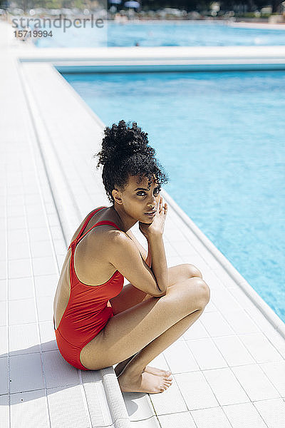 Porträt einer jungen Frau im roten Badeanzug am Poolufer sitzend